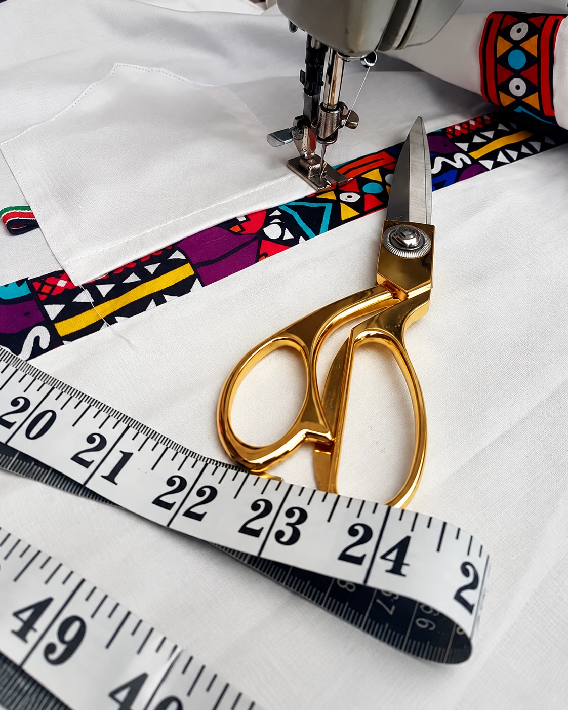 Tailor's shears and a measuring tape resting on white fabric beside patterned trim.