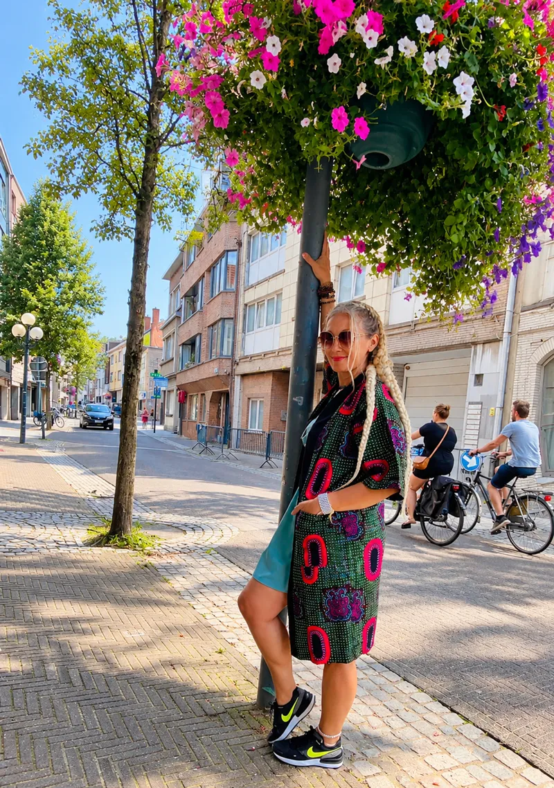 Customer in a green and pink print co-ord set and sunglasses, leaning against a lamppost on a flower-lined street